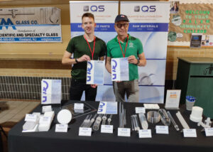 Joel Johnson, Sales Manager of Quartz Solutions Inc., and Norbert, CEO of GVB GmbH - Solutions in Glass, at their booth at ASGS Symposium 2024 showcasing glassblowing innovations.
